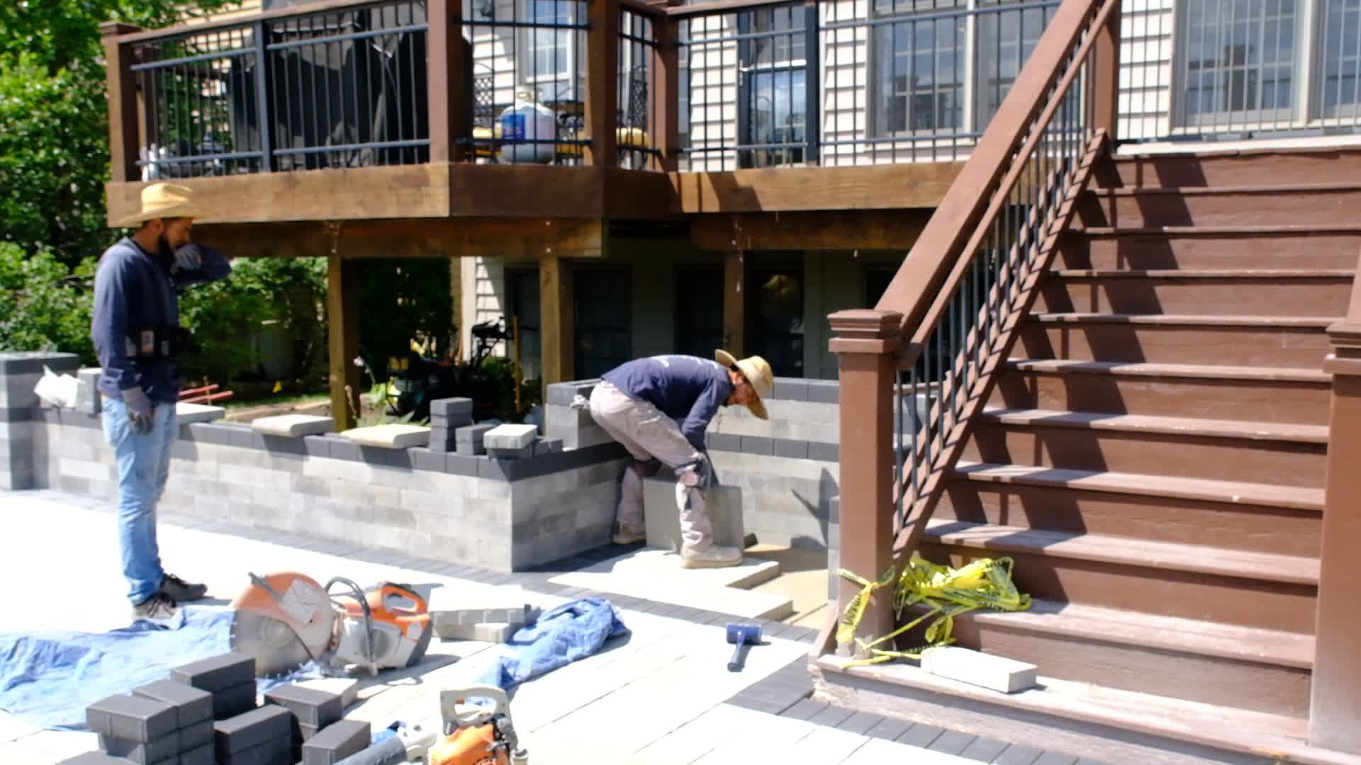 Crew building a paver seating wall beside deck stairs